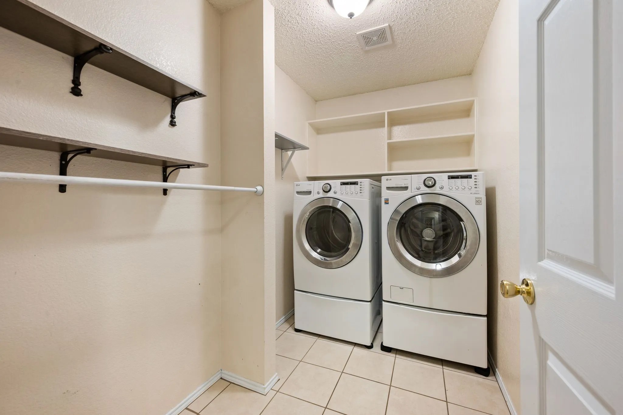 Dedicated laundry area featuring front-loading appliances, white cabinetry, and a clothing rod with wood-finish shelving