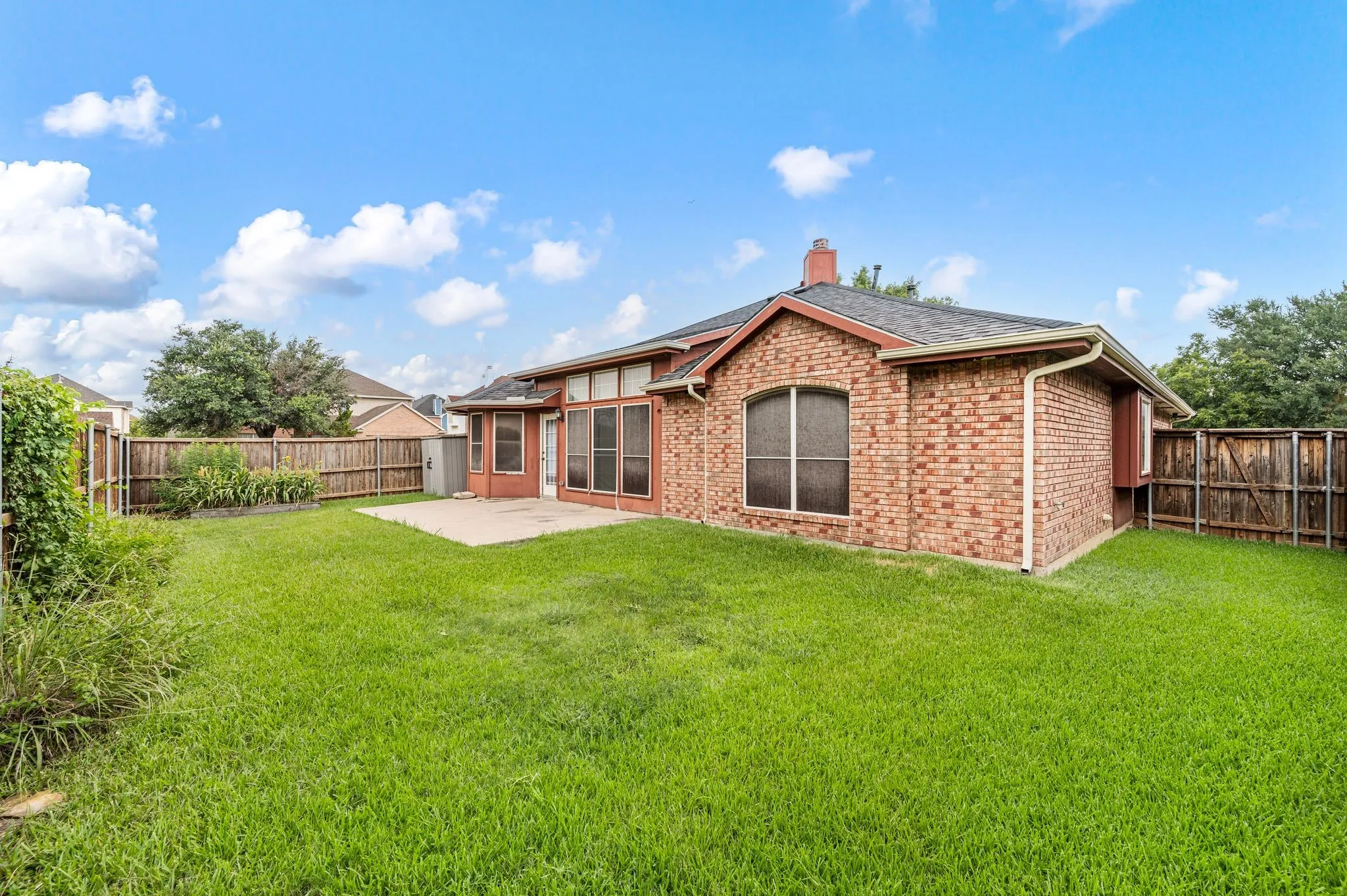 Expansive backyard featuring a lush lawn, a concrete patio, a brick exterior, and a wood privacy fence
