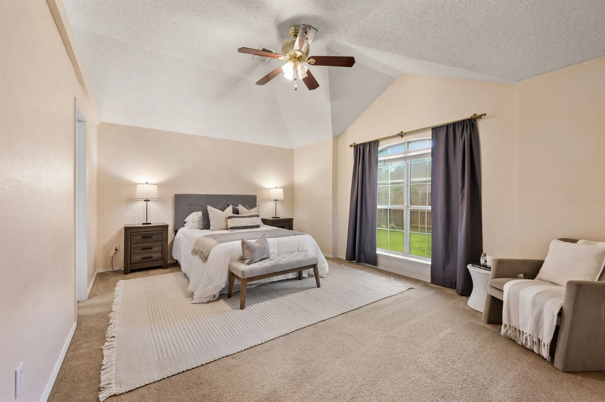 Vaulted ceiling bedroom featuring carpeting, a large window with backyard greenery, and a ceiling fan with integrated lighting