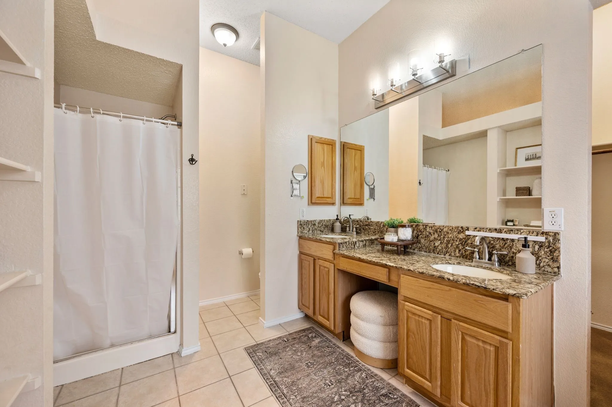 Bathroom featuring dual undermount sinks with chrome fixtures, granite countertops, and light wood cabinetry