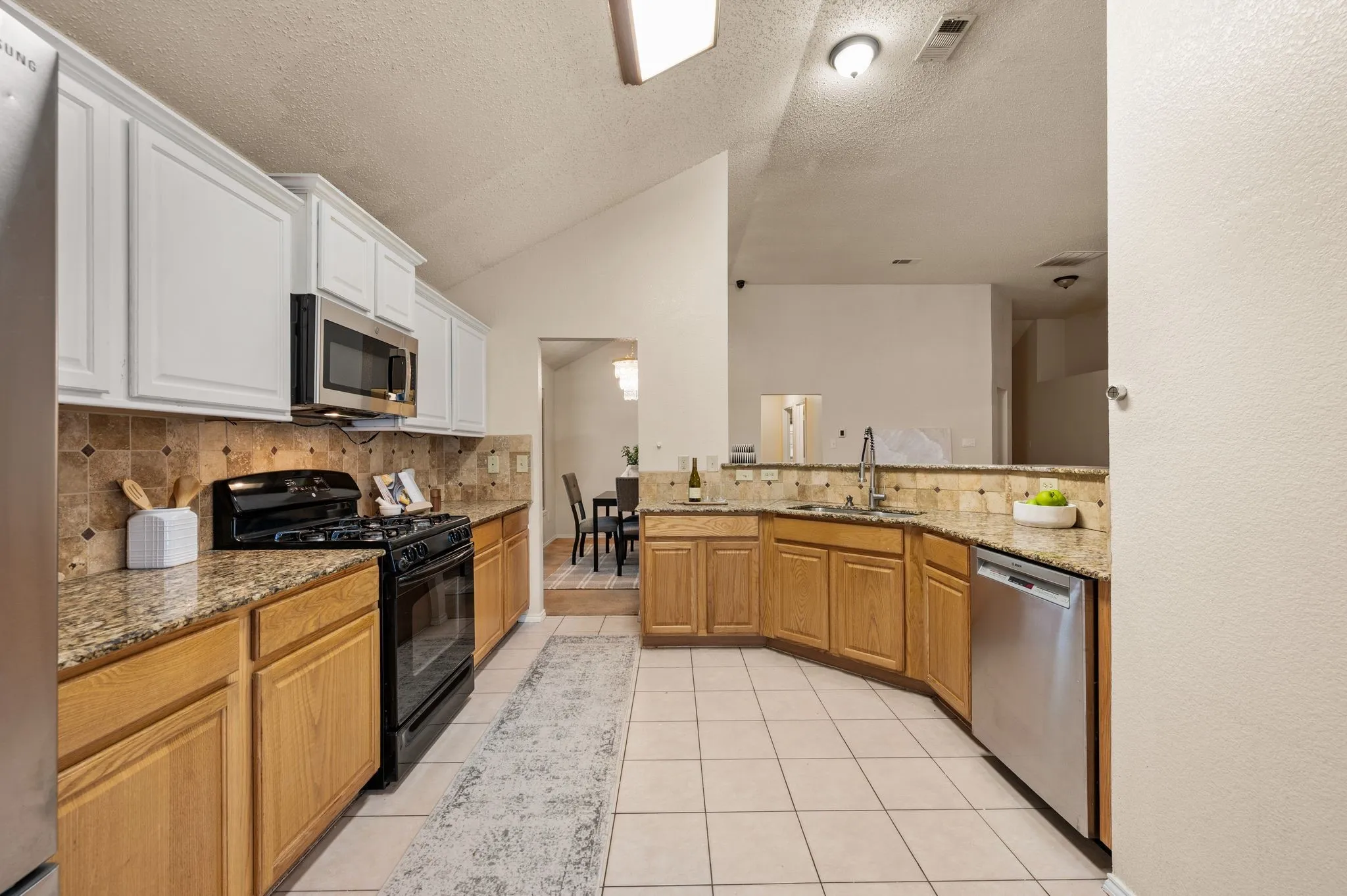 Spacious kitchen featuring a vaulted ceiling, U-shaped countertops, stainless steel appliances, a tile backsplash, and light wood cabinetry