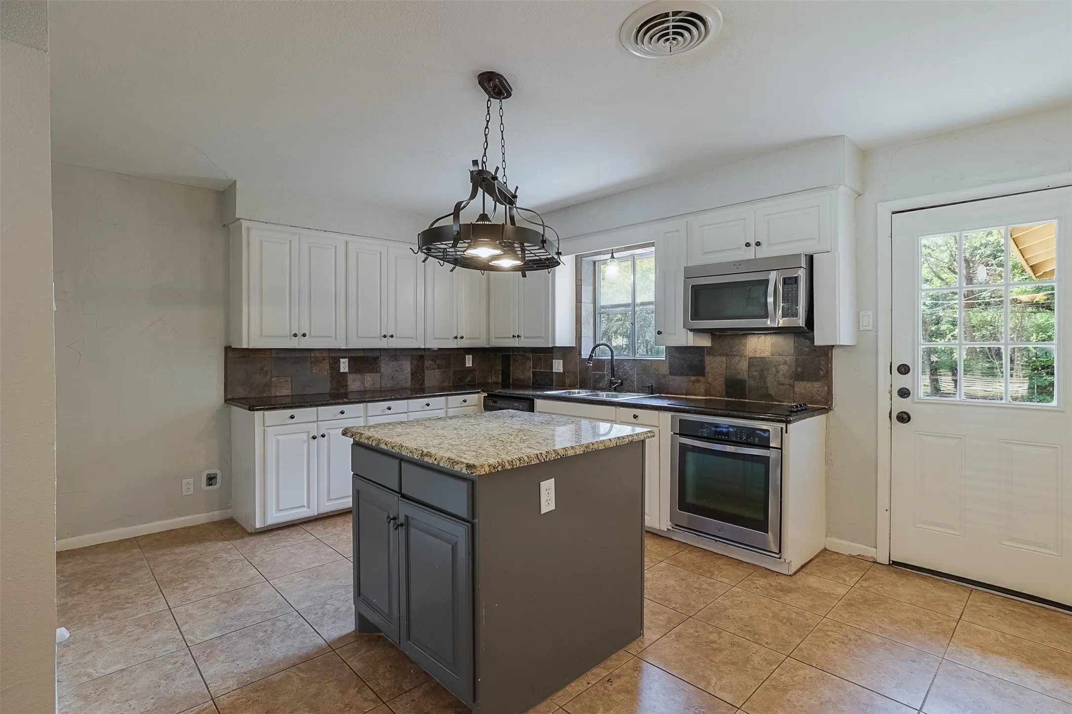 Kitchen featuring white cabinetry, a central island with a stone-finish countertop, tile flooring, and stainless steel appliances