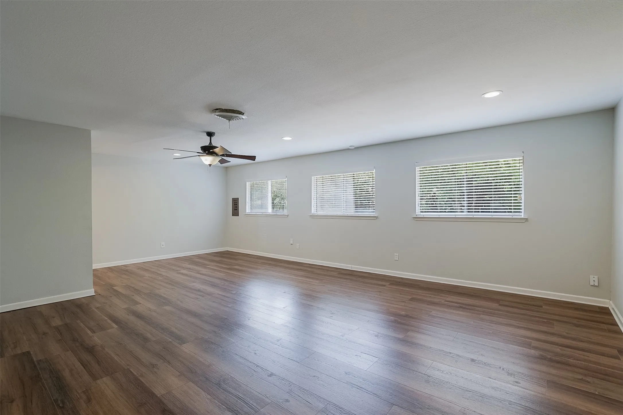 Spacious interior with wood-finish flooring, light gray walls, multiple windows with blinds, recessed lighting, and a ceiling fan with integrated light