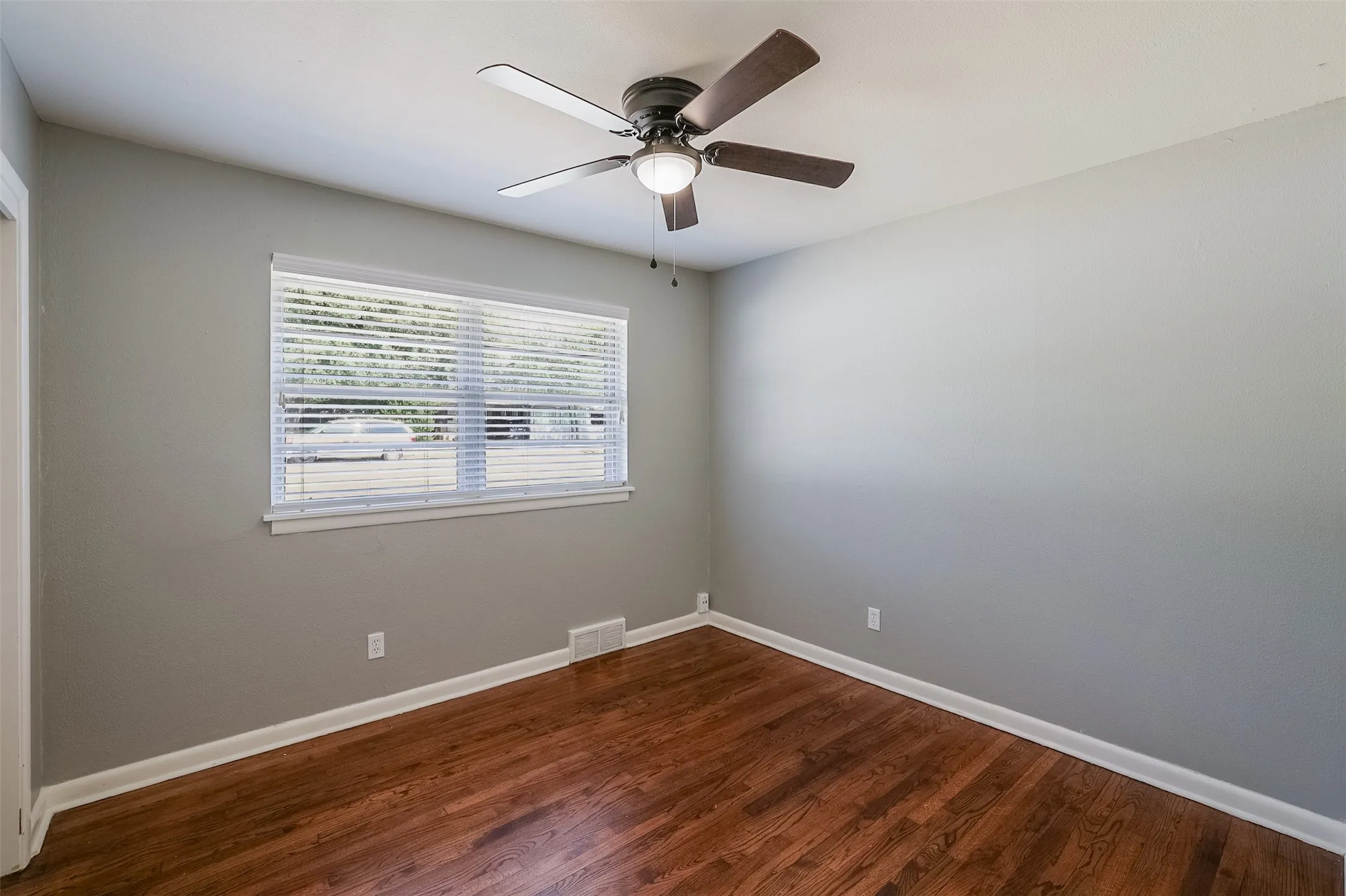 Rich wood-finish flooring, white trim, and a ceiling fan with integrated lighting