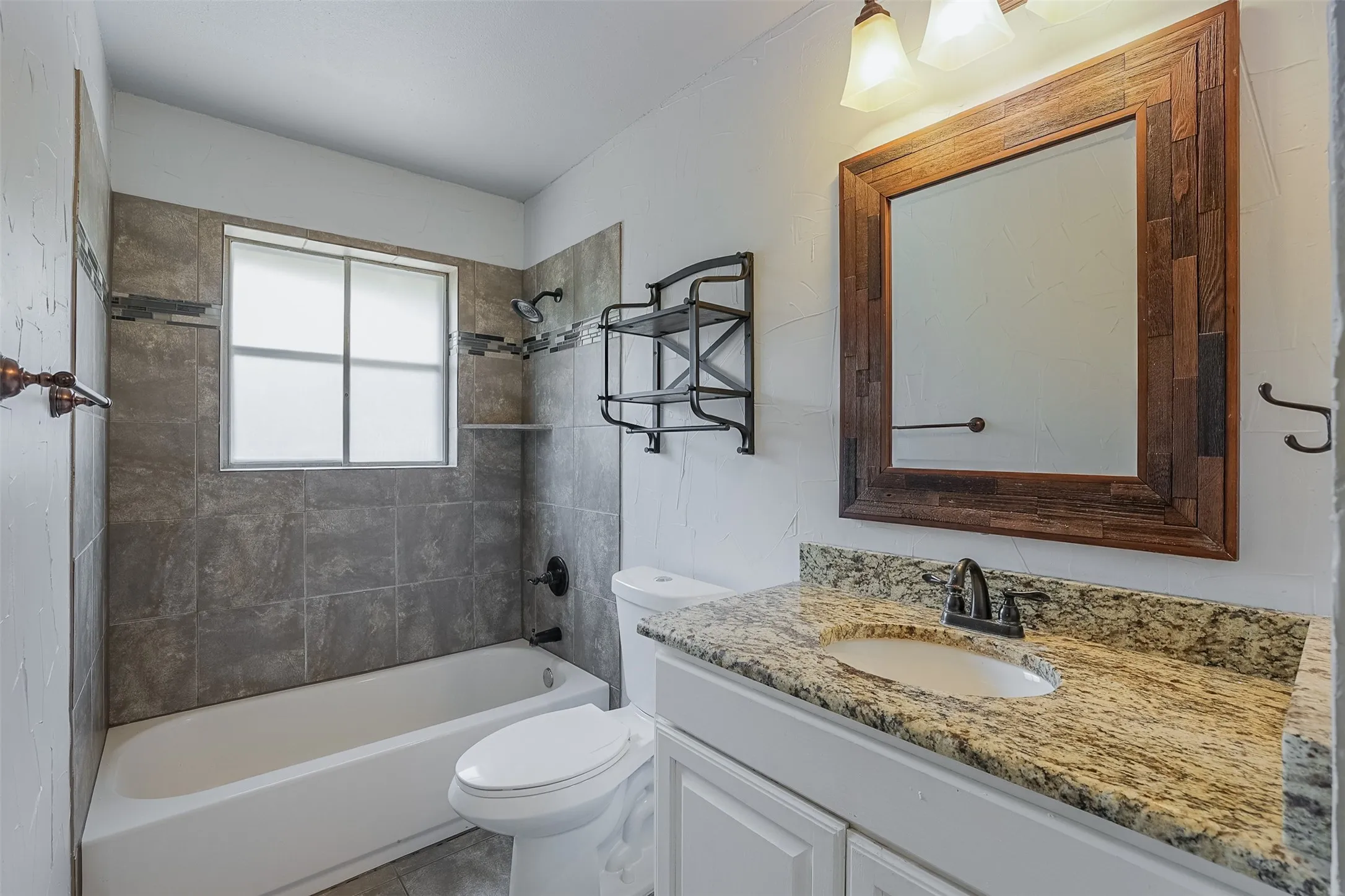 Bathroom featuring a granite-style countertop, integrated sink, wood-framed mirror, and a tiled shower/tub combination with a built-in shelf