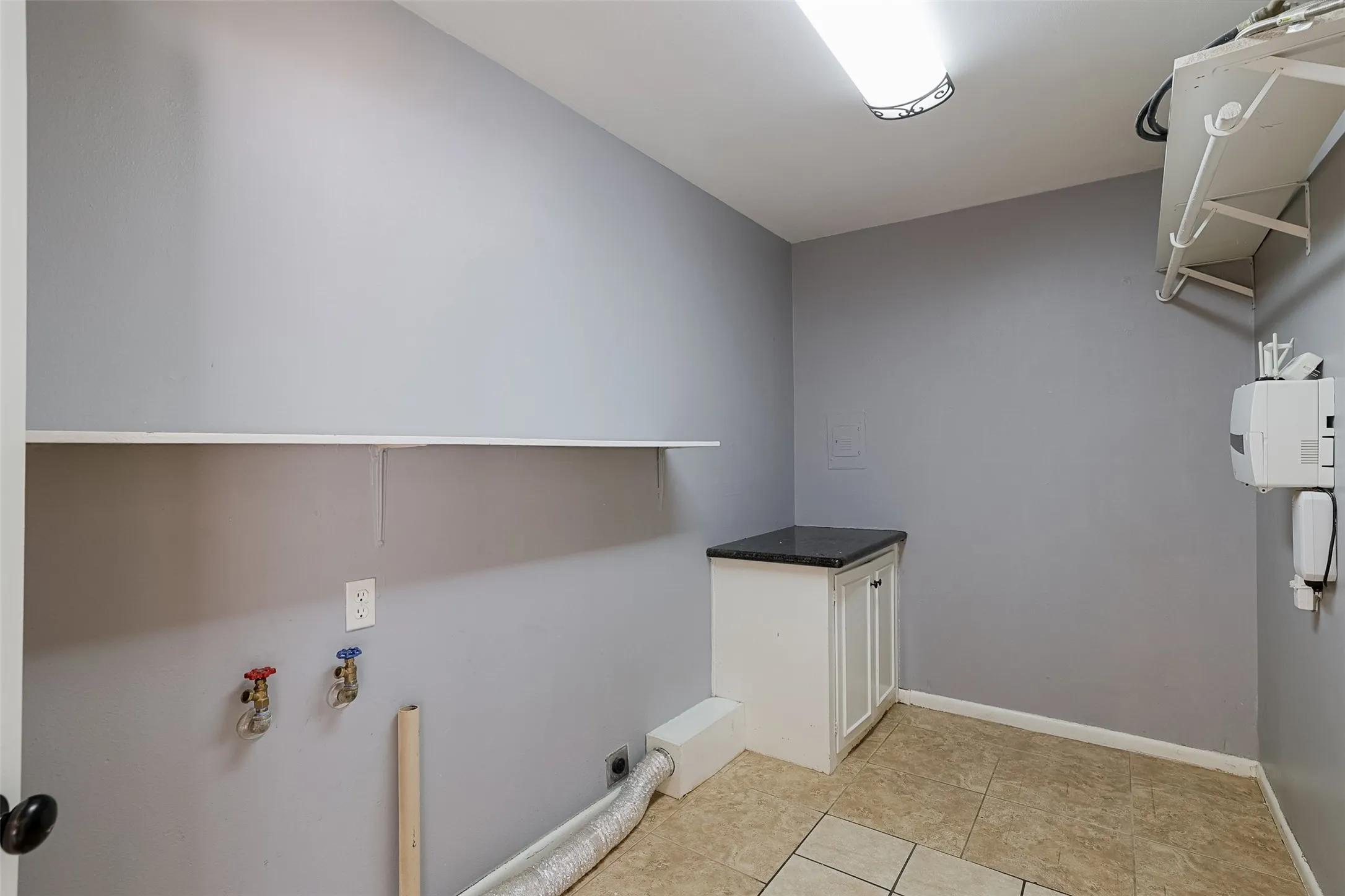 Utility space featuring a built-in shelf, tiled flooring, white cabinetry with a dark countertop, and overhead lighting