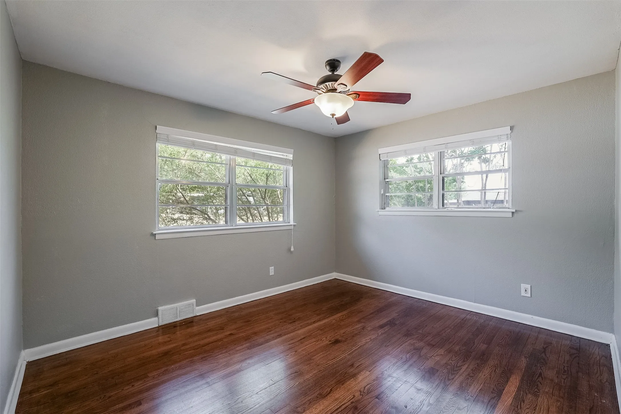 Hardwood flooring, painted walls, two windows, and a ceiling fan with integrated lighting
