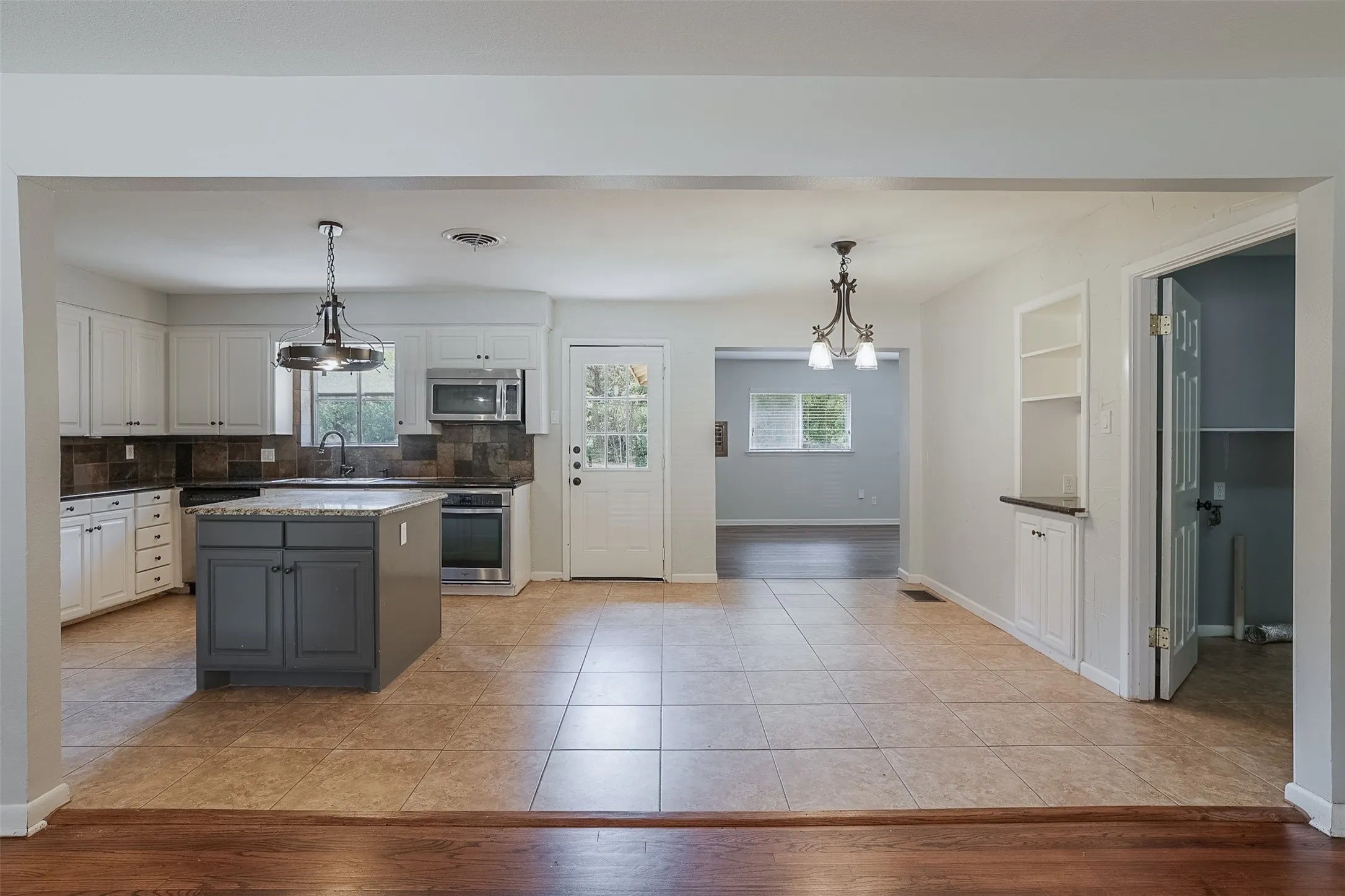 Kitchen featuring a central island with gray cabinetry, white perimeter cabinetry, stainless steel appliances, and a tiled backsplash