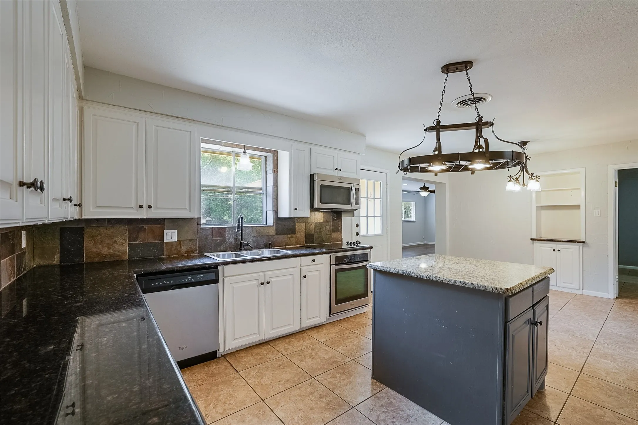 Kitchen featuring white cabinetry, stone tile backsplash, dark countertops, a central island with a lighter countertop, and tile flooring