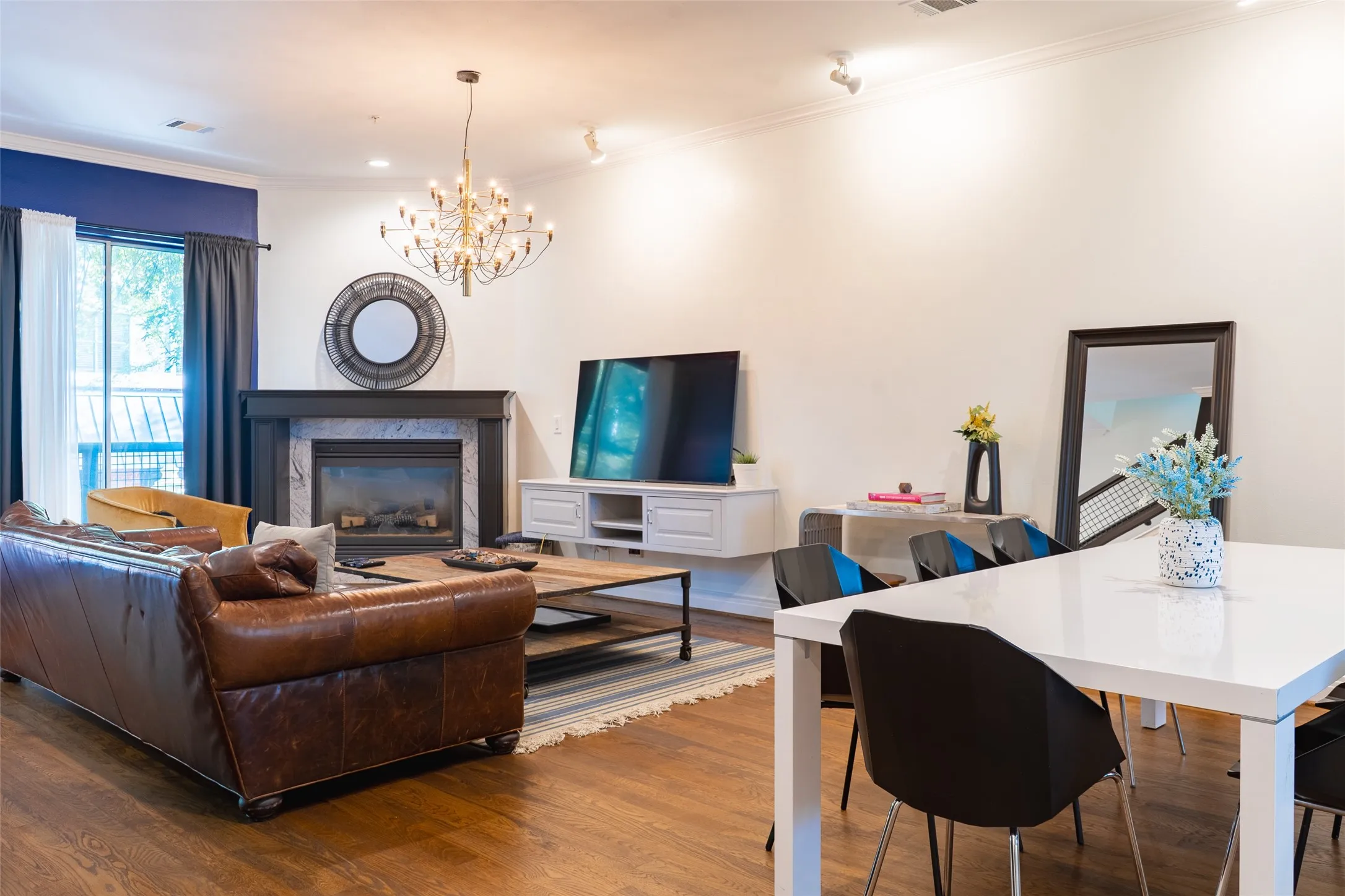 Spacious living area featuring wood-finish flooring, a fireplace with a stone surround and dark wood mantel, and an overhead chandelier light fixture