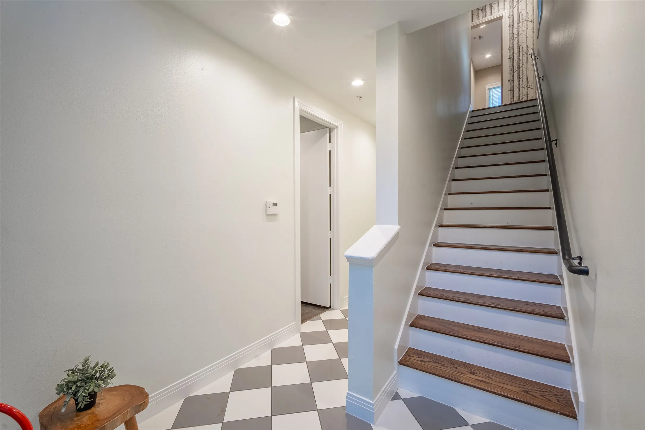 Foyer featuring a white and grey checkered tile floor, a staircase with wood-finish treads and white risers, a white newel post, and a black handrail