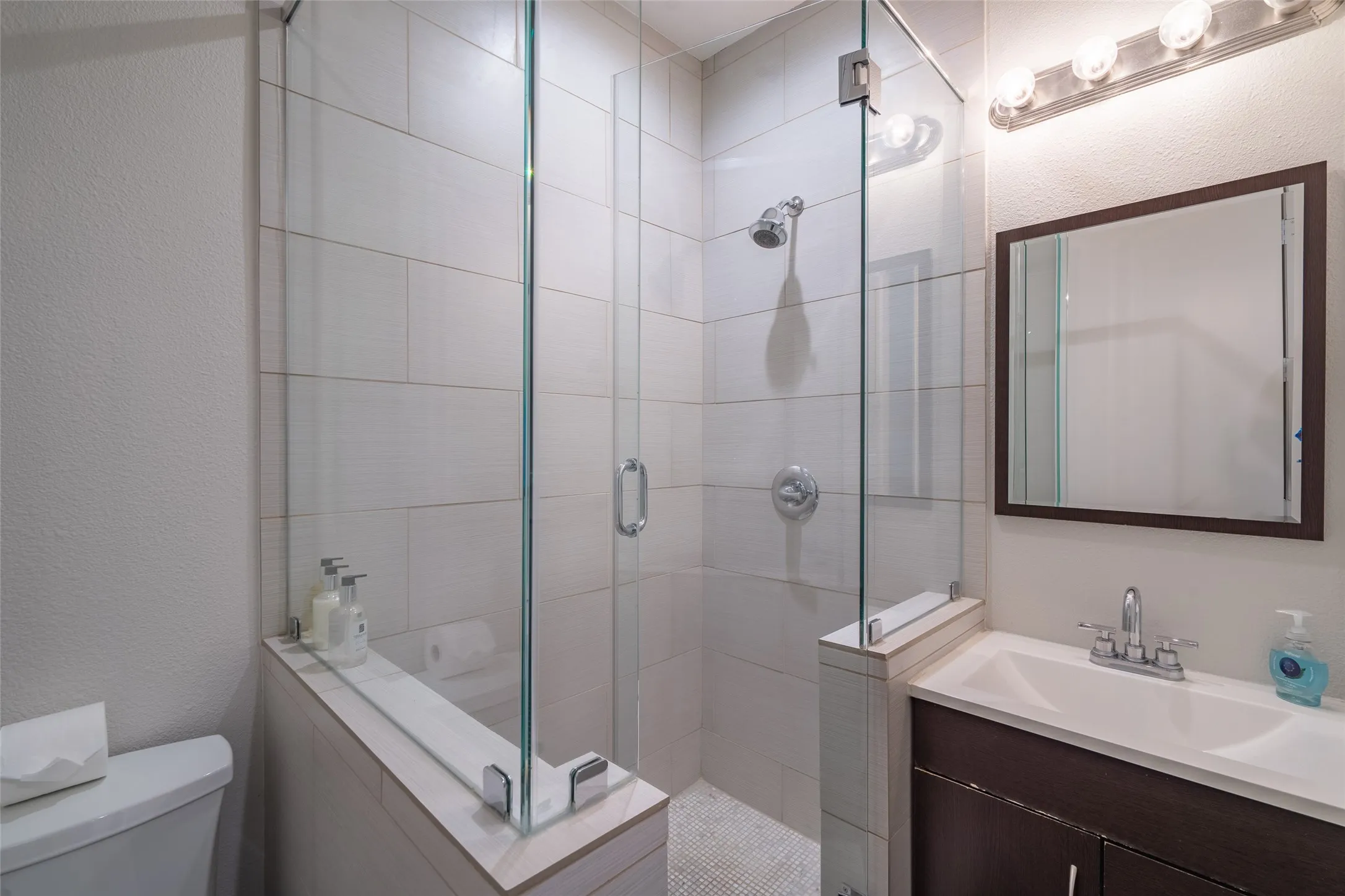 Modern bathroom featuring a glass-enclosed shower with white subway tile surround and a rainfall showerhead