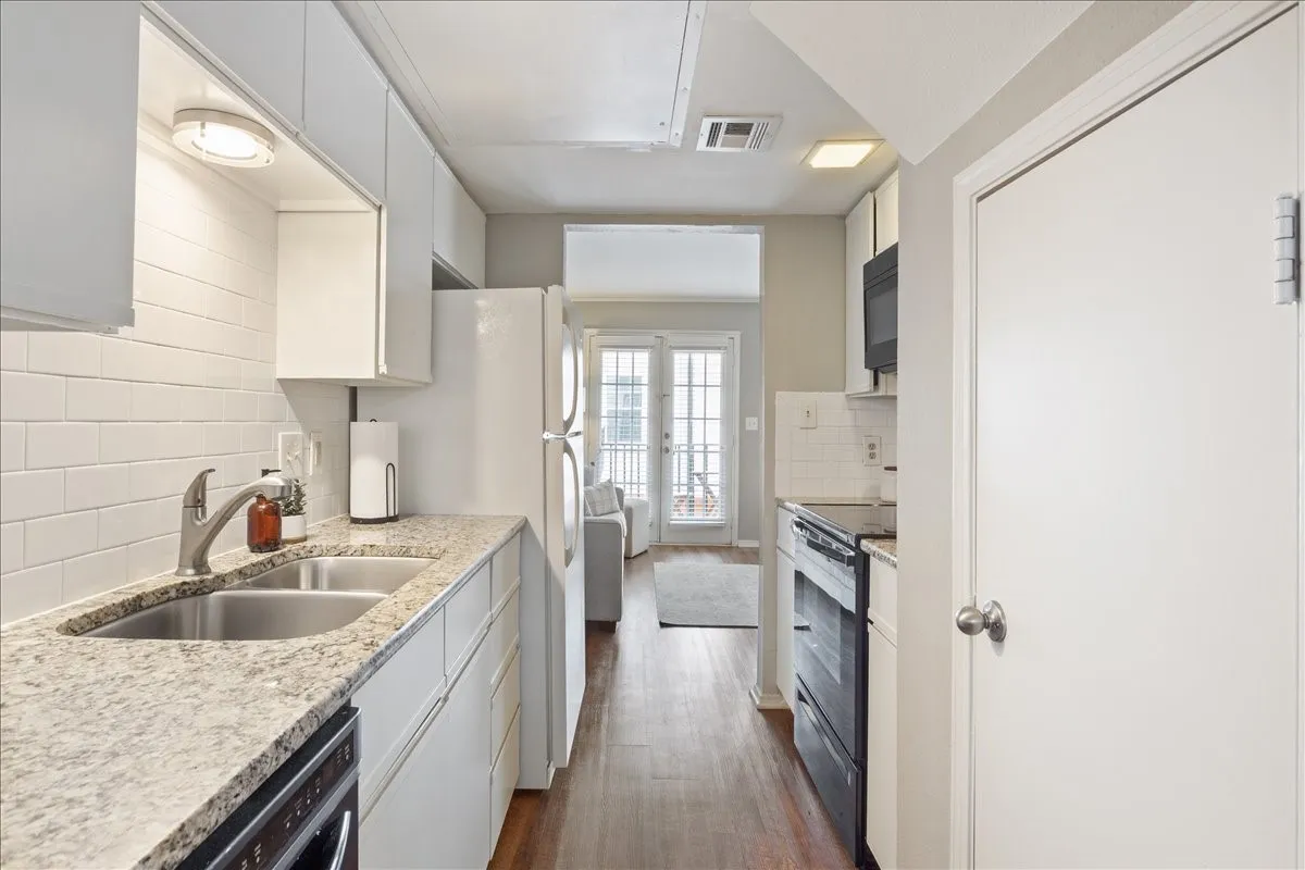 Updated kitchen with granite countertops, subway tile backsplash, white cabinetry, and generous prep space.