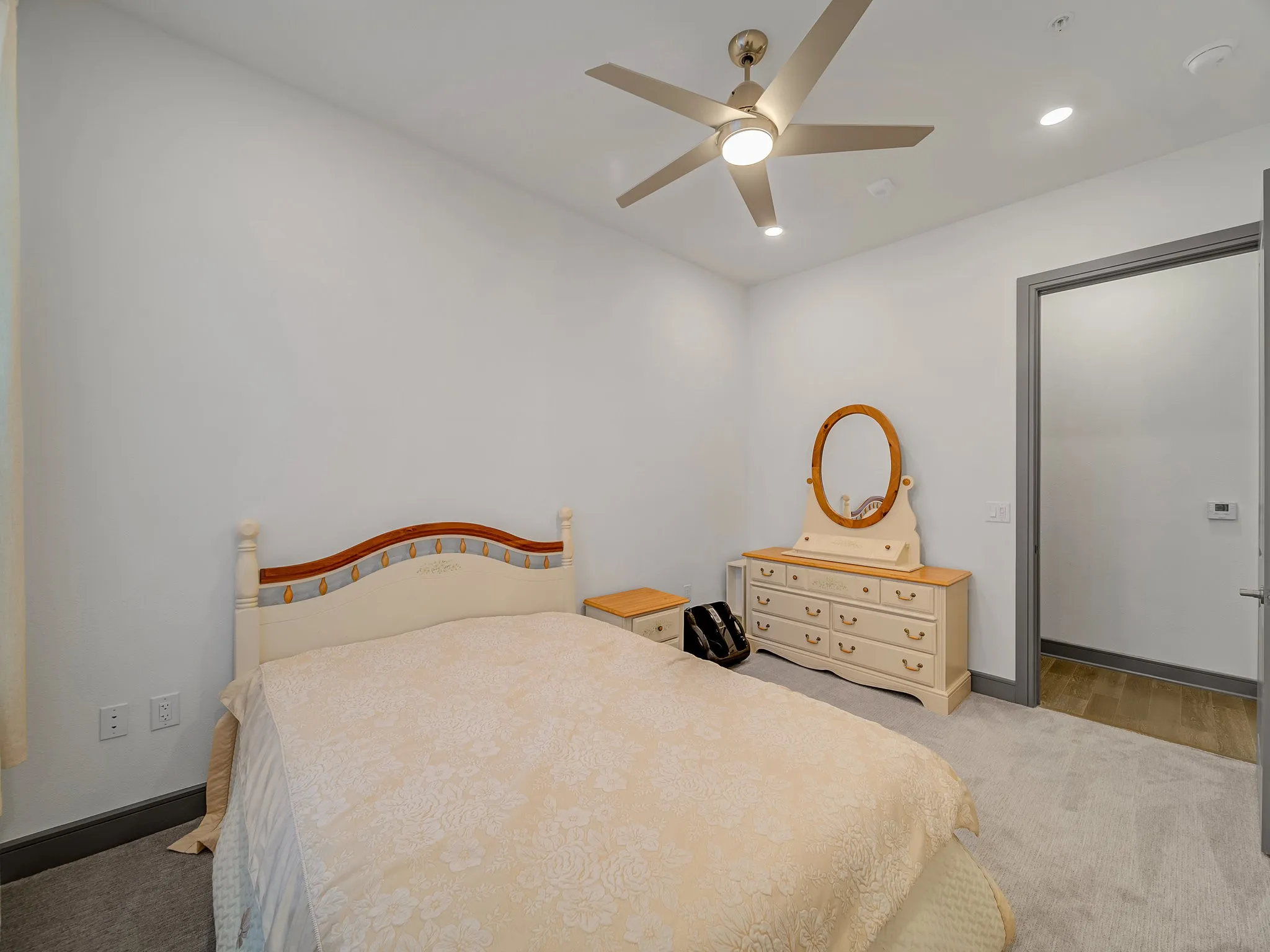 Carpeted interior space featuring a ceiling fan with integrated lighting, recessed ceiling lights, and a doorway with wood-finish flooring beyond