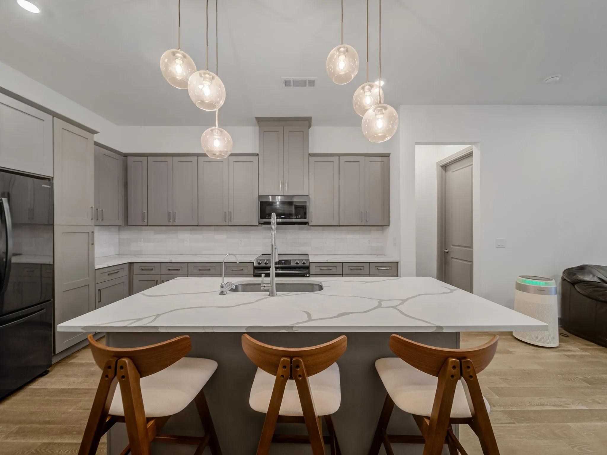 Kitchen featuring a large central island with seating, pendant lighting, light gray cabinetry, stainless steel appliances, and wood-finish flooring