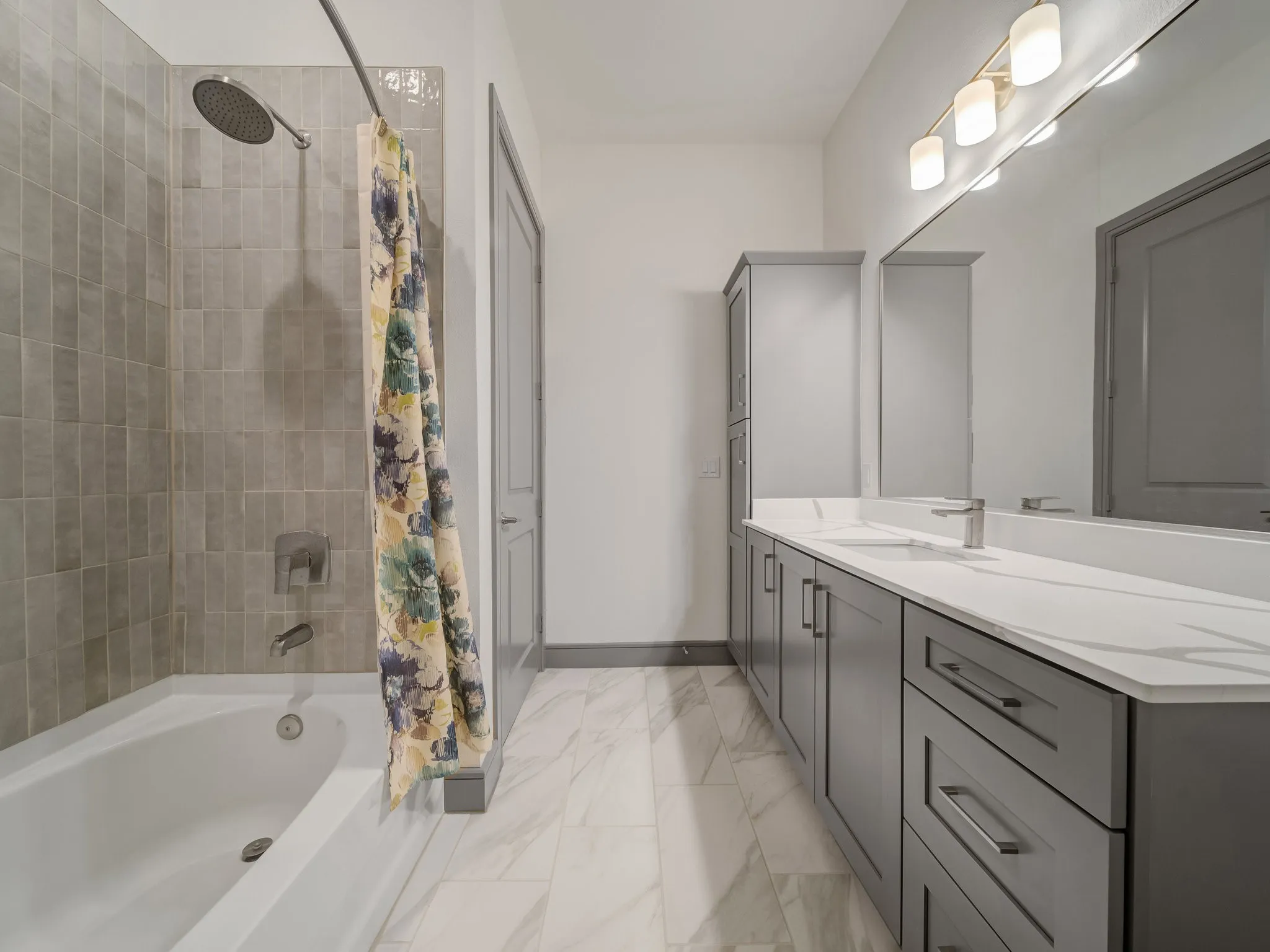 Bathroom featuring a white tub with subway tile surround, rainfall showerhead, and a vanity with dual sinks