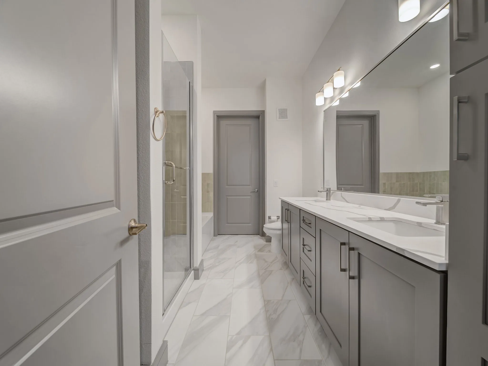 Bathroom featuring a double vanity with gray cabinetry and white countertops, a large vanity mirror with overhead lighting, a glass-enclosed shower, and marble-look floor tiling