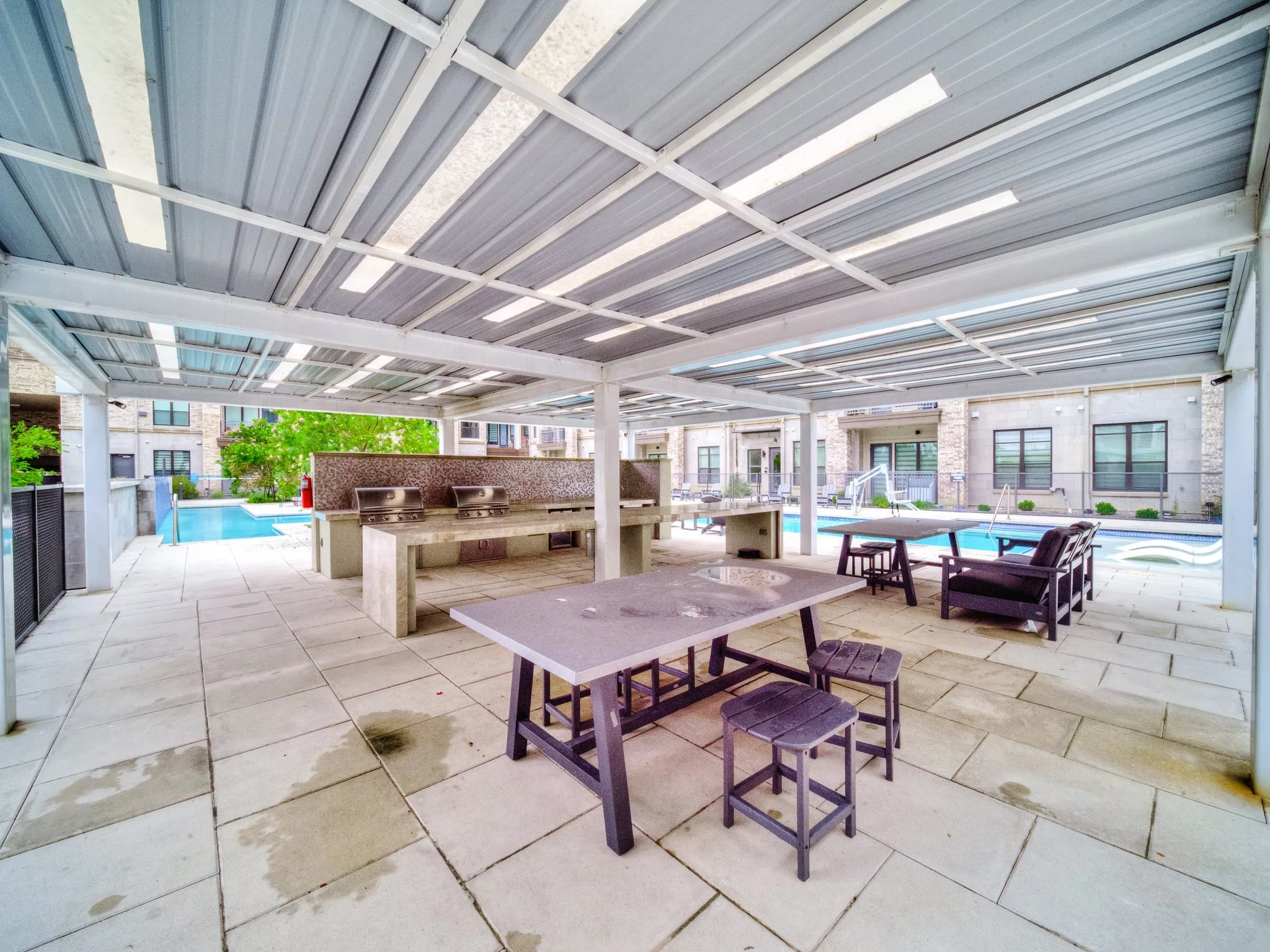 Covered outdoor patio with a metal roof structure, integrated lighting, and extensive paver flooring