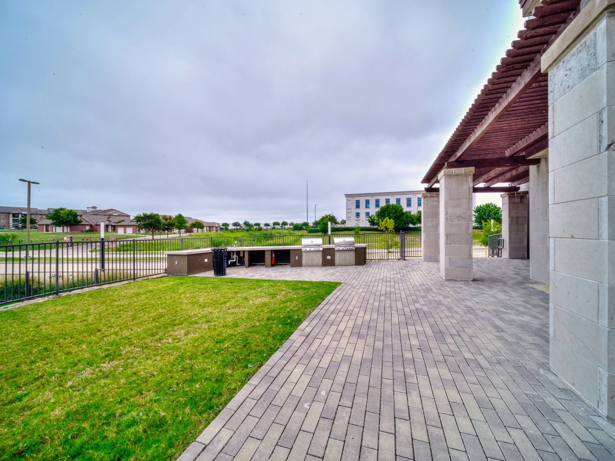 Outdoor paved patio with a wooden pergola, stone columns, and an integrated grilling station