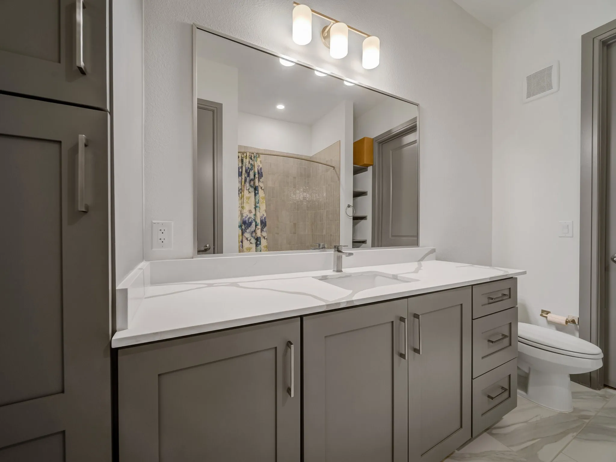 Bathroom featuring a gray vanity with shaker-style cabinetry, a white countertop, an undermount sink, and a large mirror