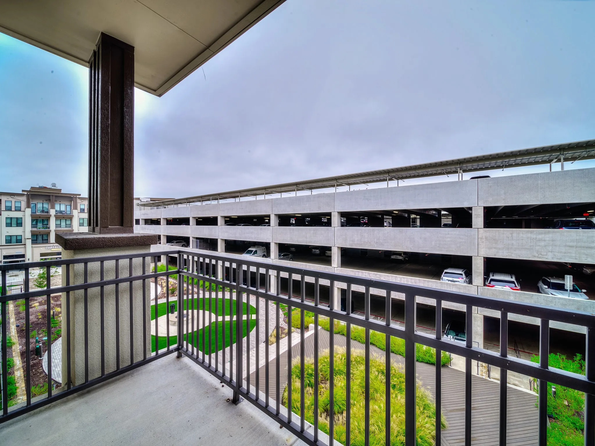 Concrete balcony with black metal railings, overlooking a landscaped courtyard with synthetic turf