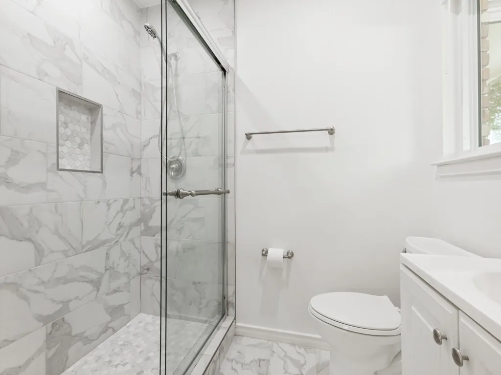 Bathroom featuring a glass-enclosed shower with marble-look tile walls and a hexagonal tile shower floor