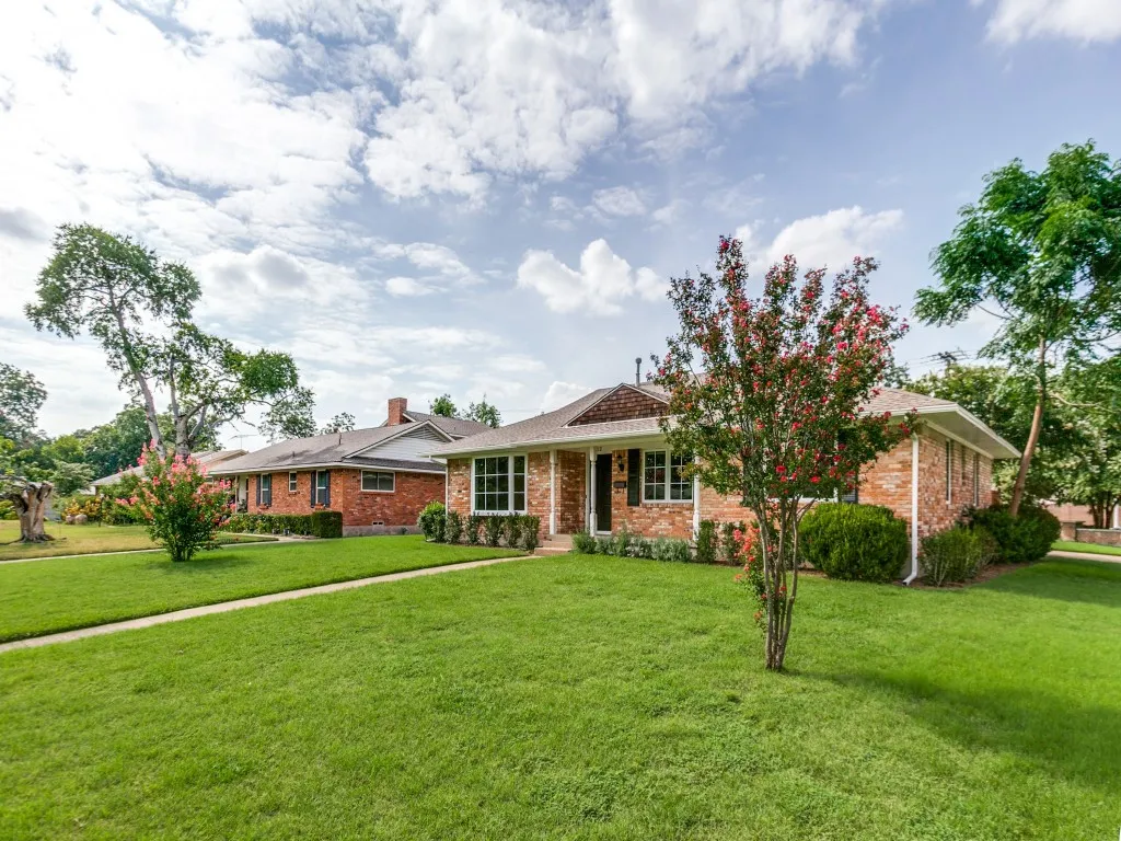 Brick exterior residence featuring a front lawn, sidewalk, mature trees, and landscaping
