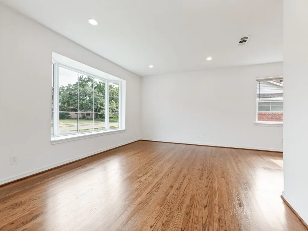 Expansive room featuring a large bay window, recessed lighting, rich wood flooring, and crisp white walls