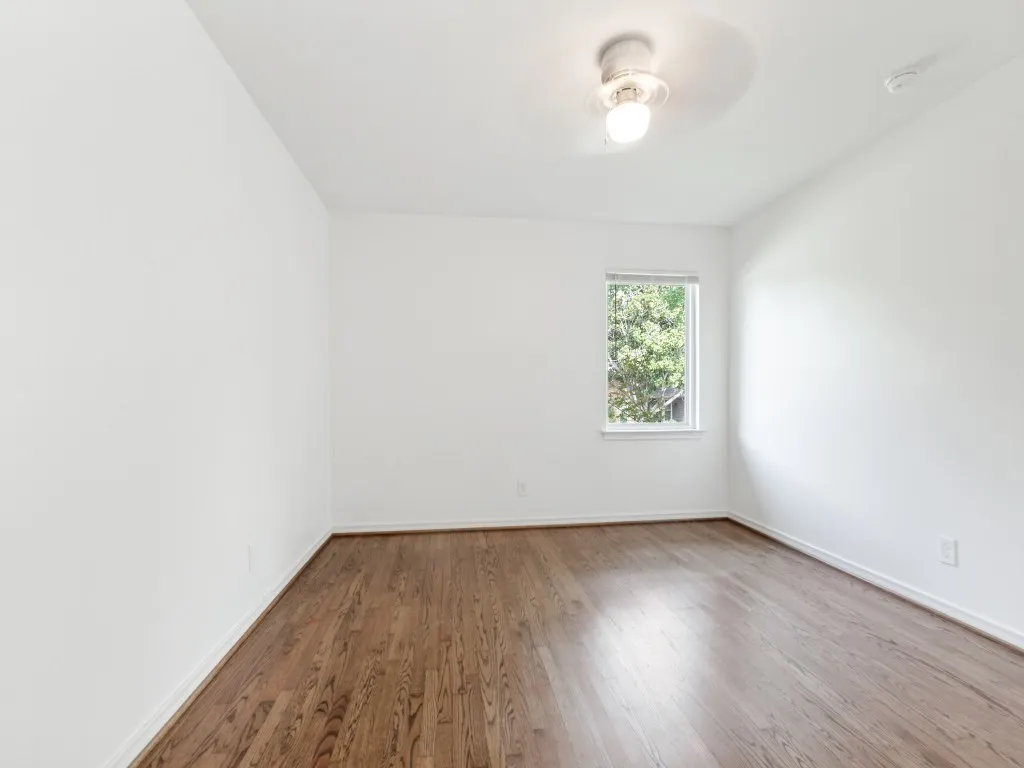 Bright room featuring wood-finish flooring, crisp white walls, a single window, white baseboards, and a ceiling-mounted light fixture