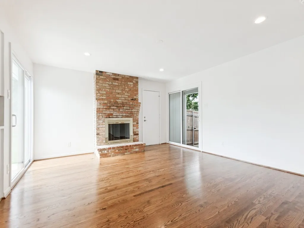 Spacious living area featuring a brick fireplace with a raised hearth, hardwood flooring, and recessed lighting