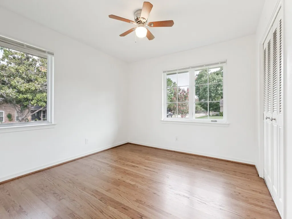 Bright interior space featuring wood-finish flooring, two large windows with white trim, a ceiling fan with light fixture, and a louvered bi-fold closet door