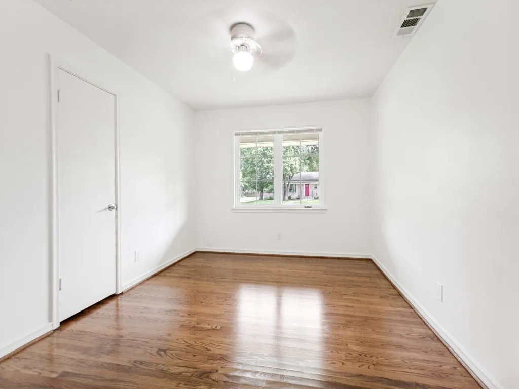 Wood-finish flooring with a satin sheen, white baseboards, and a single window with blinds