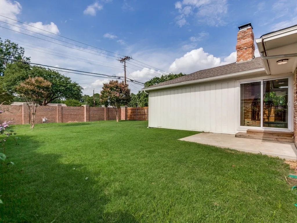 Expansive green lawn with a full brick perimeter fence and additional wood fencing