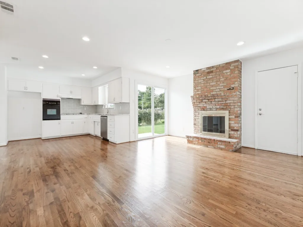 Open-concept living area featuring a brick fireplace with a stone hearth, wood-finish flooring, and a kitchen with white cabinetry and stainless steel appliances