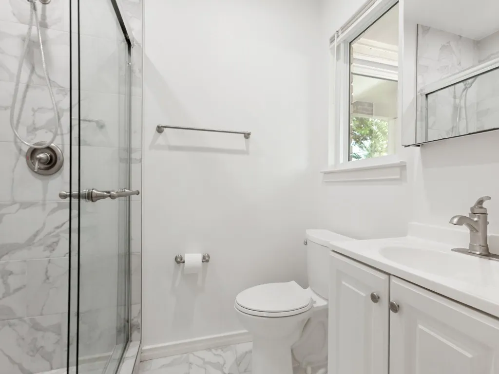 Bathroom featuring a glass-enclosed shower with marble-look wall tile, a white vanity with integrated sink, a large window, and coordinating floor tile