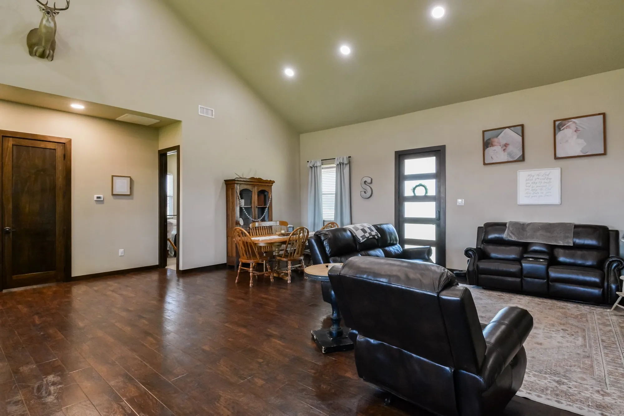 Spacious living area featuring wood-finish flooring, vaulted ceilings with recessed lighting, and dark wood trim