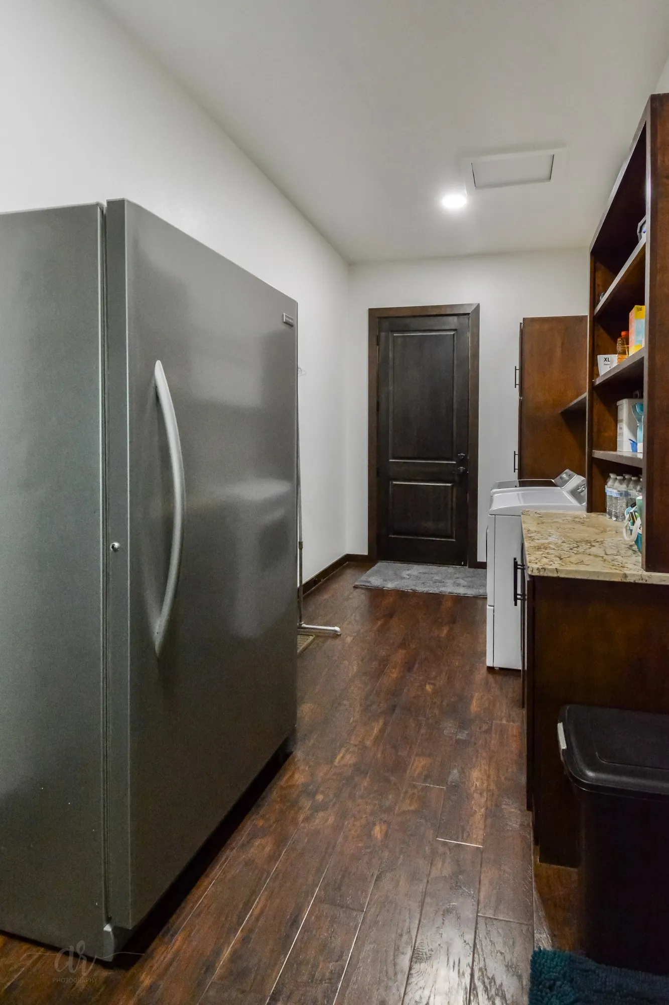 Utility room featuring wood-finish flooring, a stainless steel refrigerator, dark wood cabinetry with open shelving, a built-in countertop, and a dark paneled door