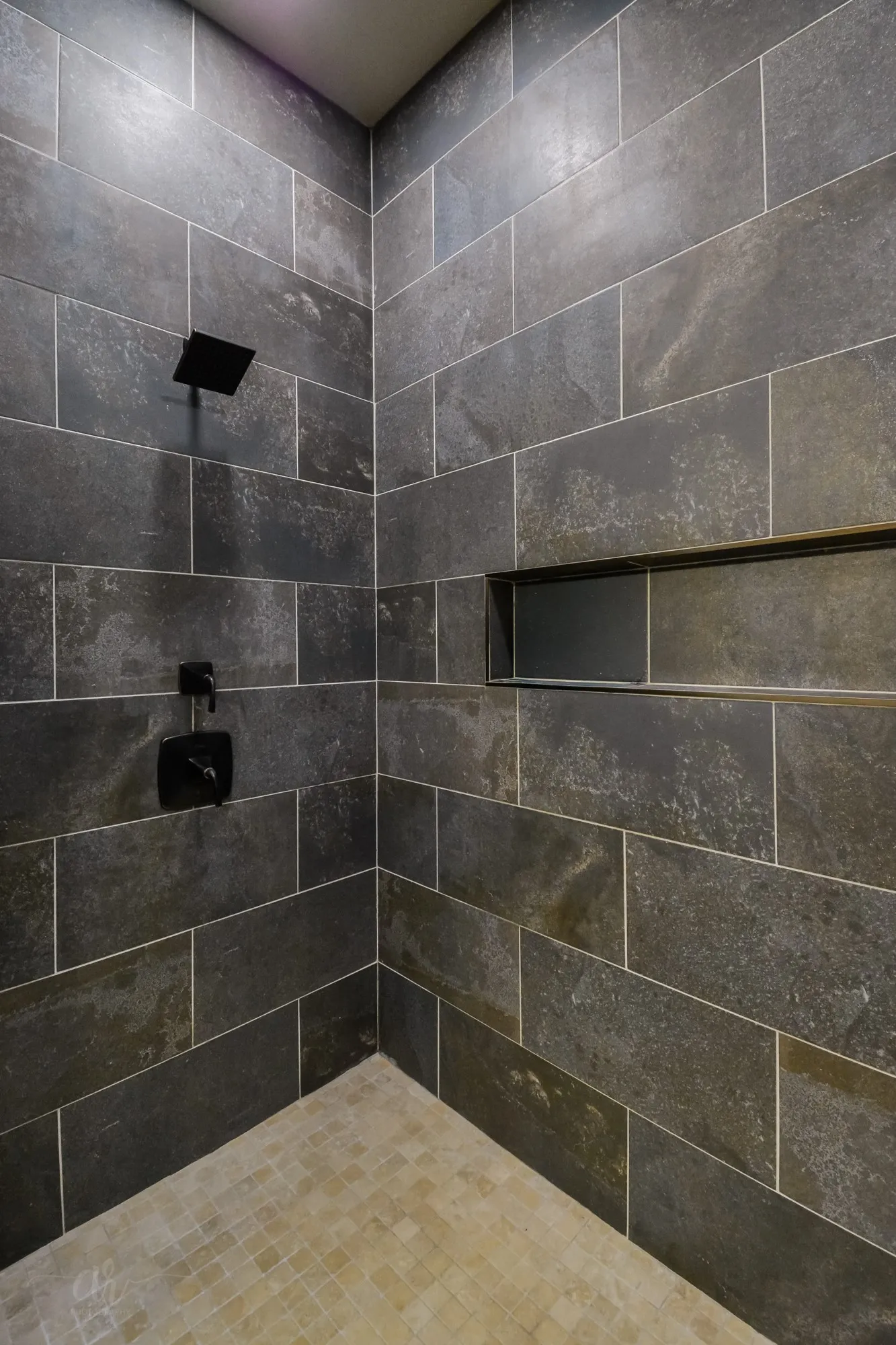 Shower enclosure featuring dark rectangular wall tiles and a light-toned mosaic floor