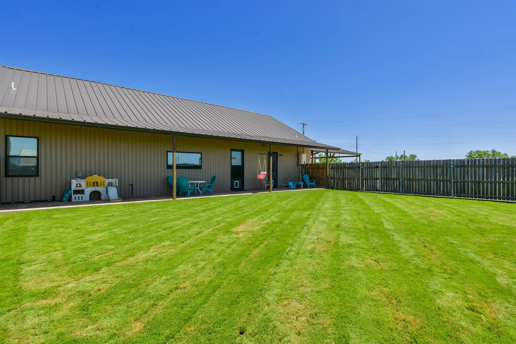 Expansive lawn featuring a privacy fence, covered patio, and metal siding exterior with a matching metal roof