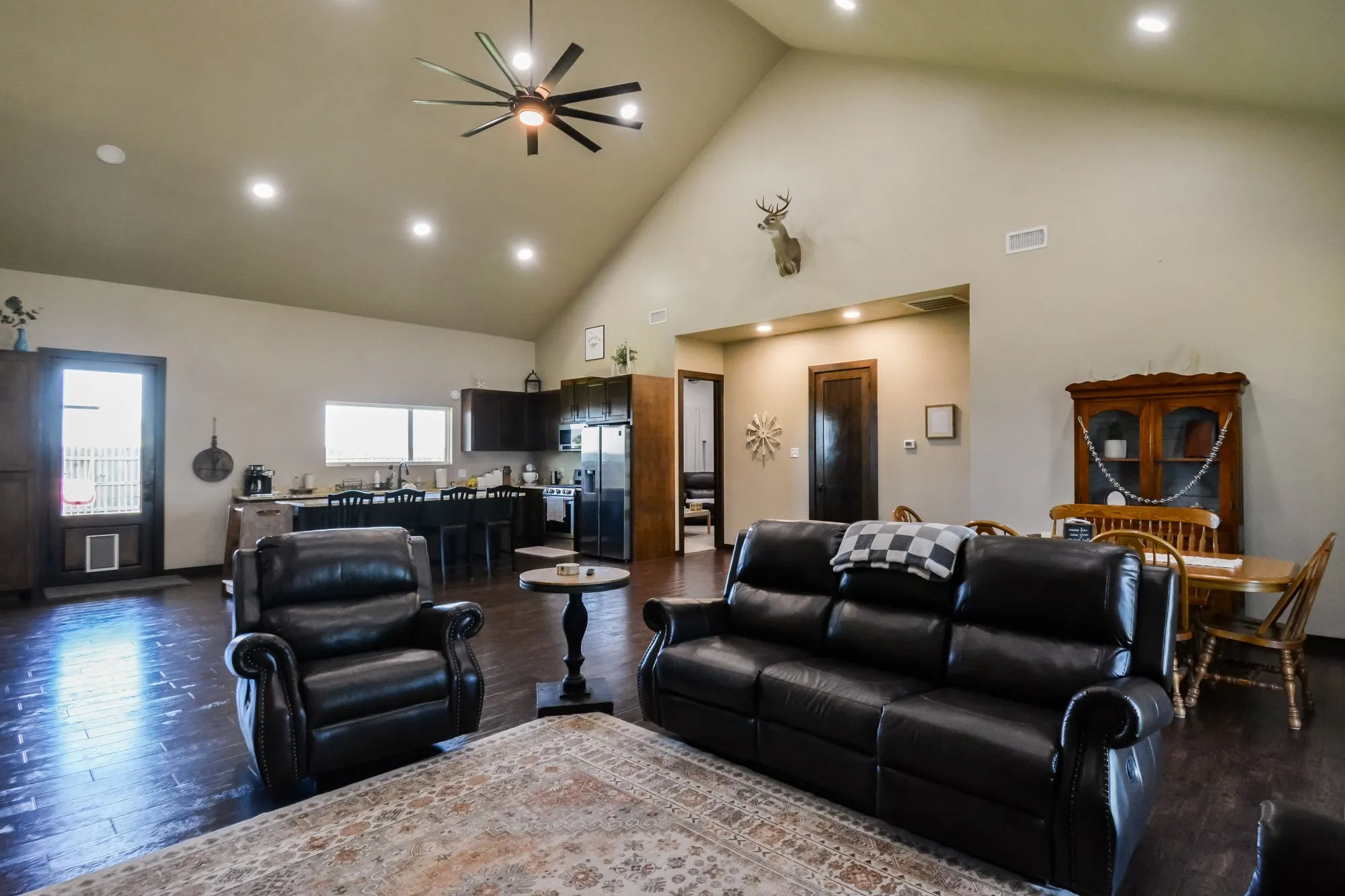 Vaulted ceiling with recessed lighting and ceiling fan, dark wood-finish flooring, kitchen featuring dark cabinetry and stainless steel refrigerator, dining area with wood hutch, and dark interior doors