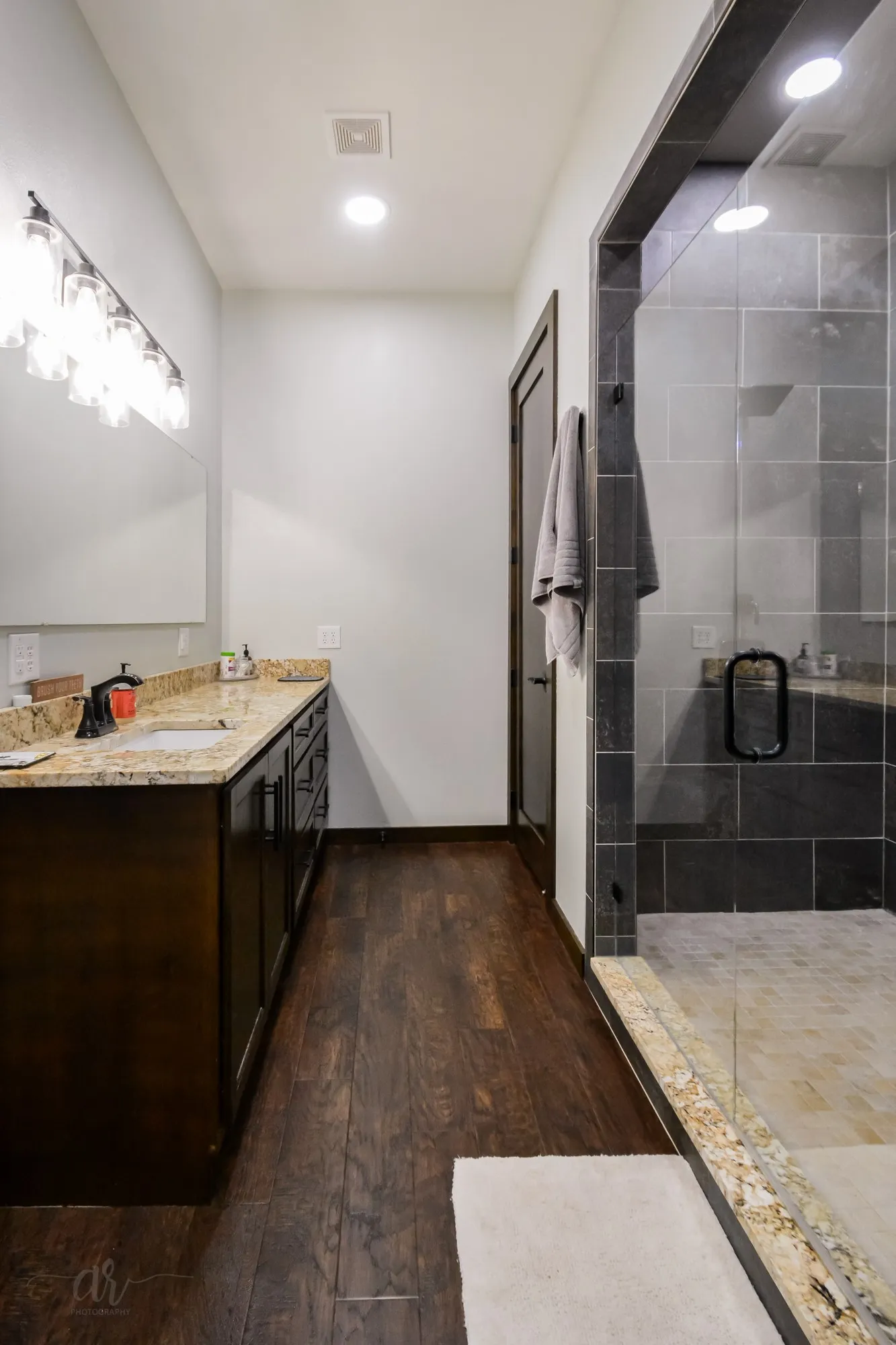 Spacious bathroom featuring a dual vanity with a stone countertop, dark wood-finish cabinetry, and wood-finish flooring