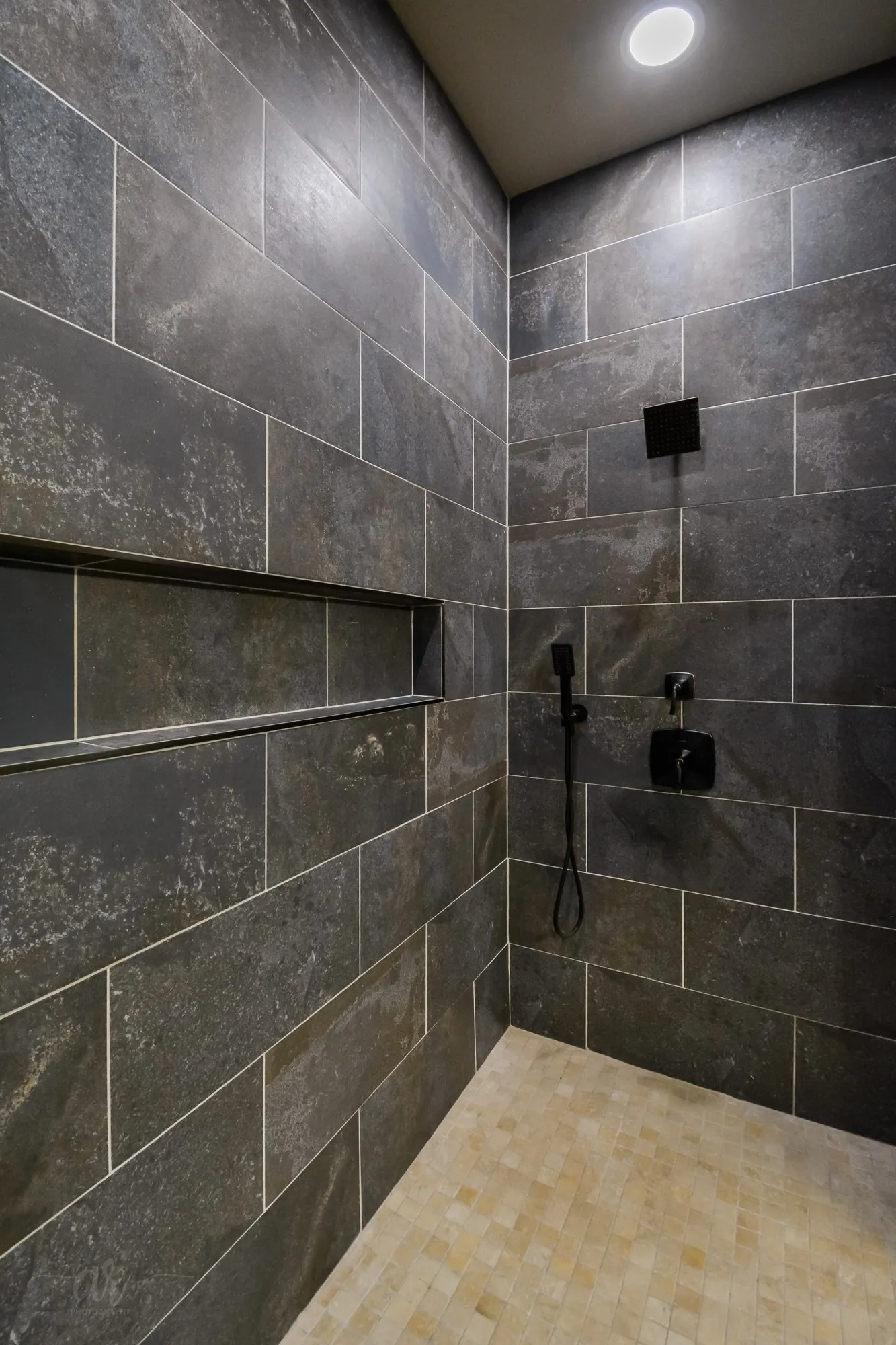 Tiled shower with dark rectangular wall tiles and light square floor tiles