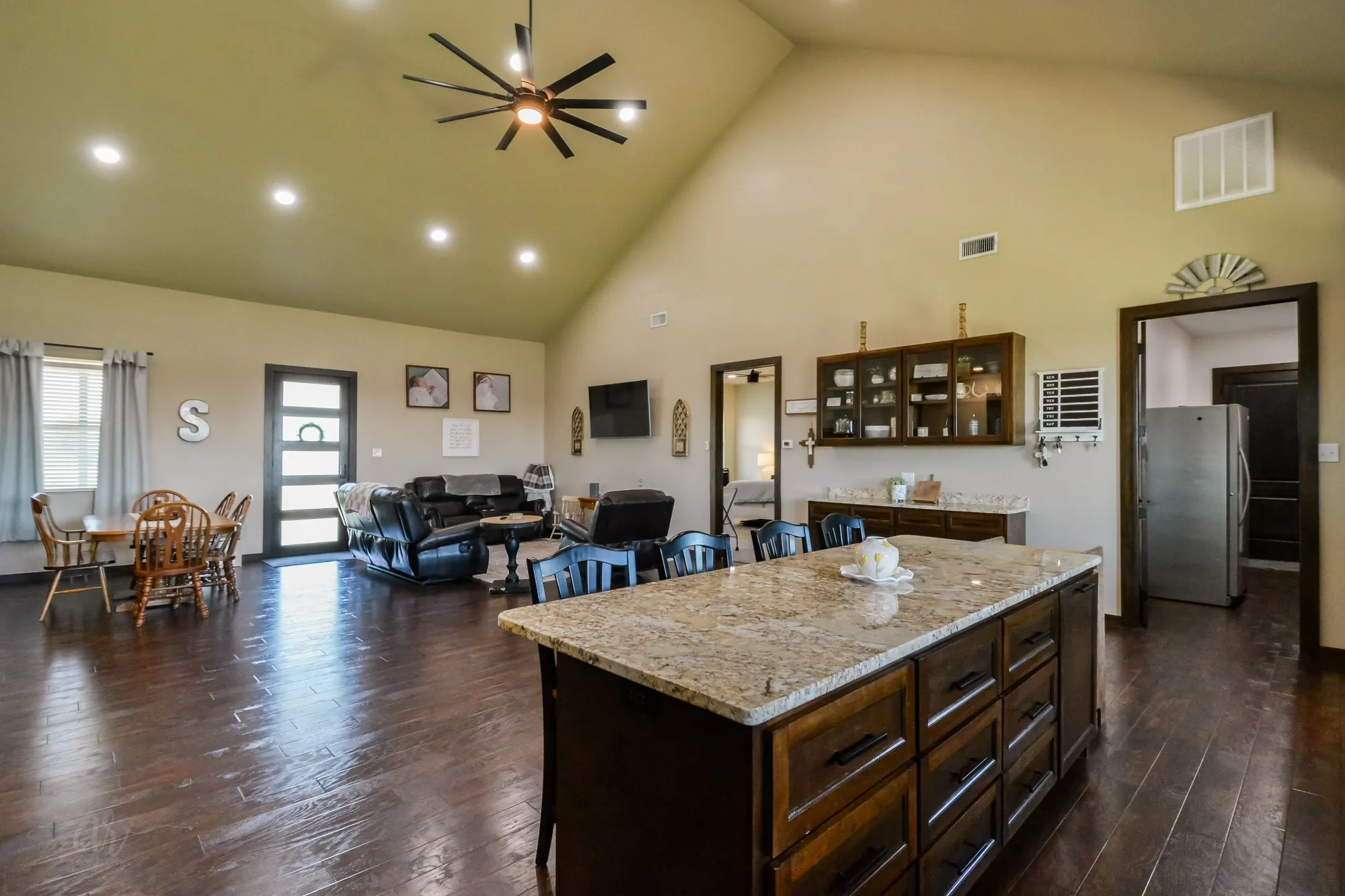 Spacious open-concept interior featuring vaulted ceilings, recessed lighting, wood-finish flooring, a kitchen island with stone countertop, and built-in cabinetry