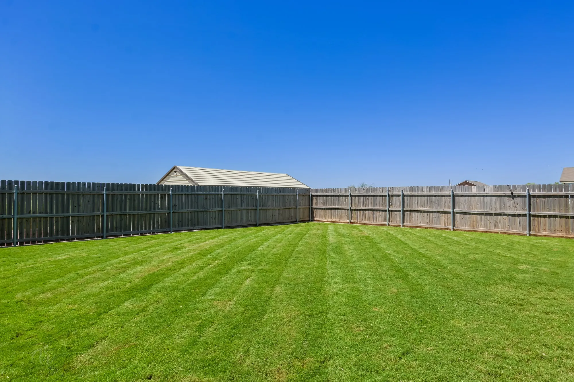 Expansive backyard featuring a lush green lawn and perimeter wood fencing