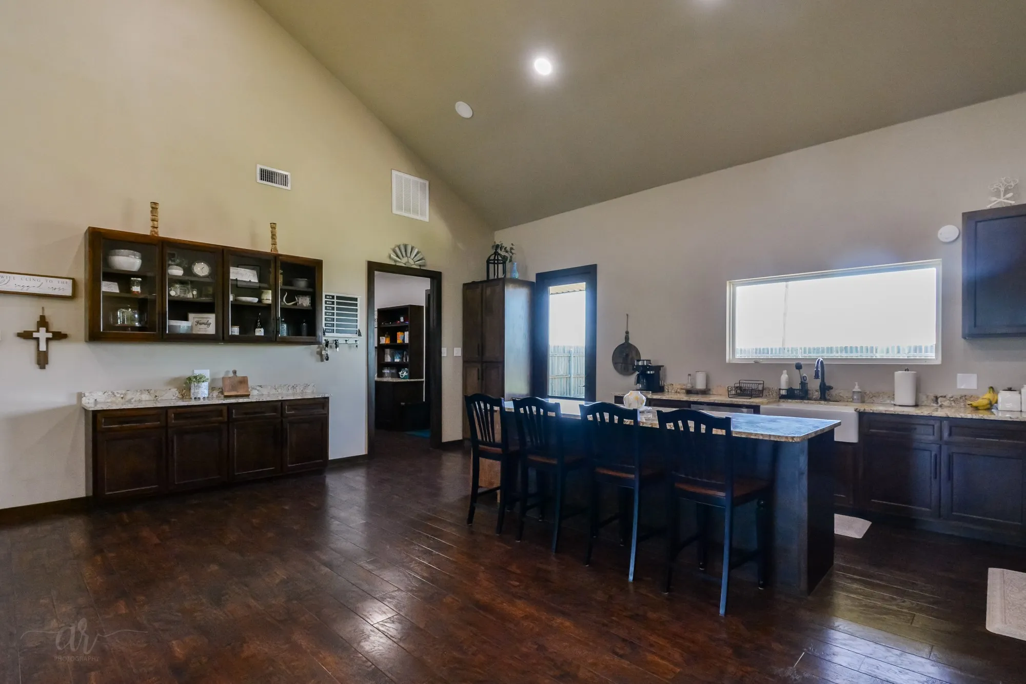Open-concept kitchen featuring wood-finish flooring, vaulted ceilings, recessed lighting, a kitchen island with seating, and a farmhouse sink