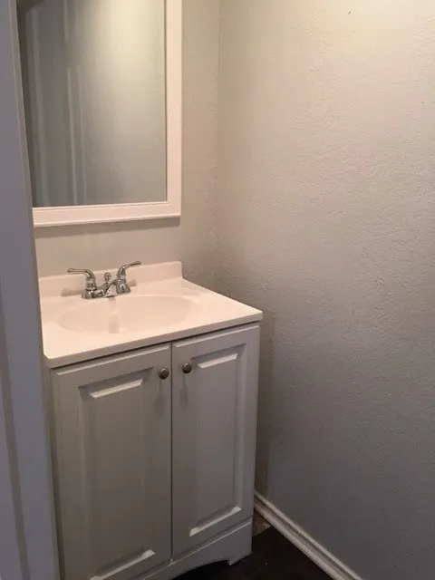 White framed mirror over a vanity with a ceramic basin, chrome faucet, and panel-front cabinetry, all set against light-colored walls and dark flooring