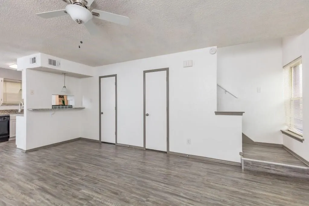 Spacious living area featuring wood-finish flooring, a ceiling fan, and a pass-through to the kitchen with a granite-style countertop