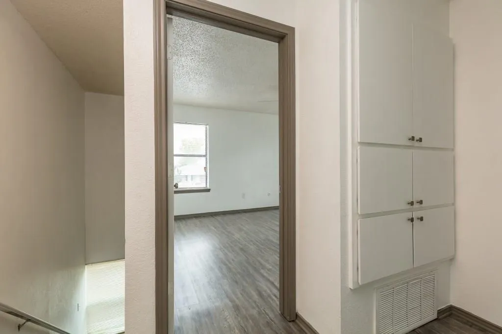 Hallway with built-in cabinetry, wood-finish flooring, and a doorway leading to a room with a window