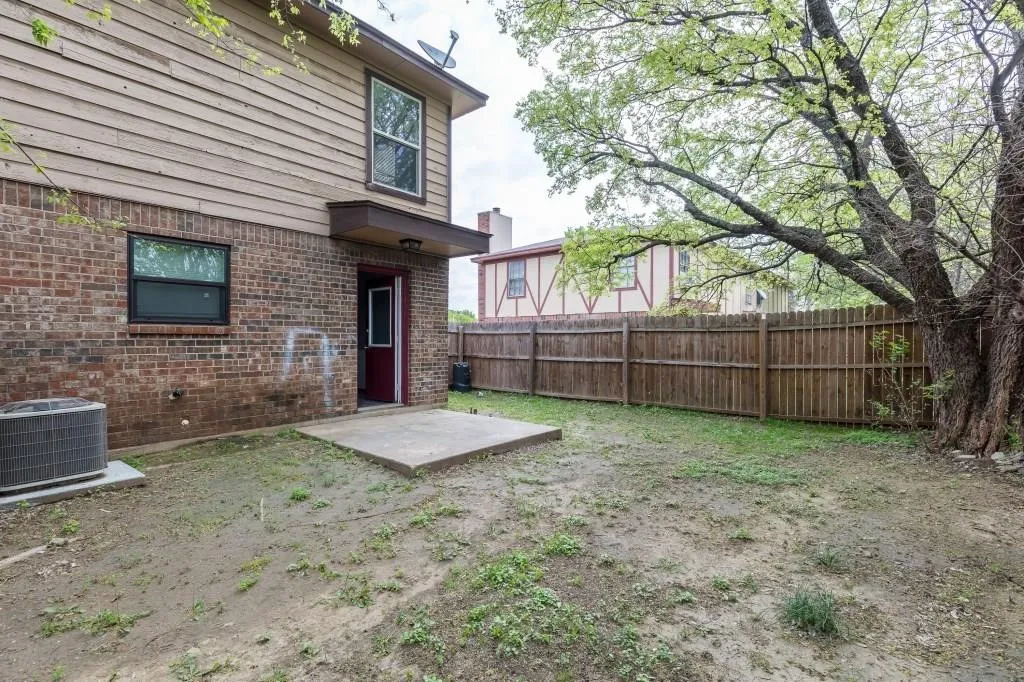 Expansive outdoor space featuring a concrete patio, brick and siding exterior, a privacy fence, and mature trees