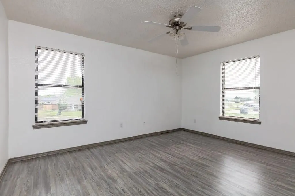 Spacious room featuring wood-finish flooring, white walls, and two windows with blinds